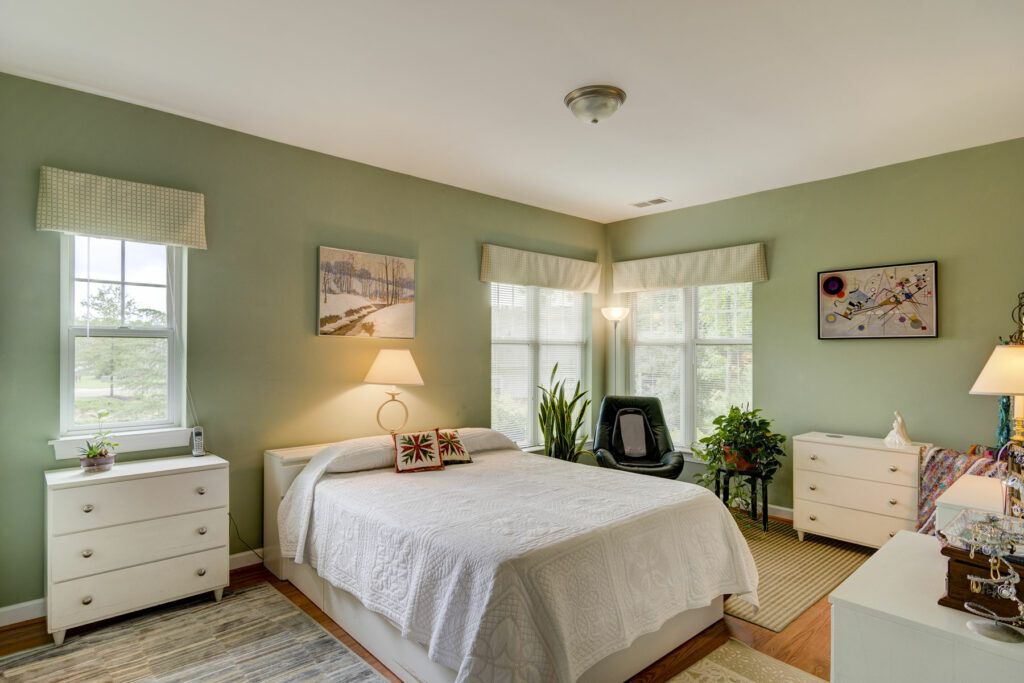 A cozy bedroom featuring a neatly made bed, large windows, and indoor plants.