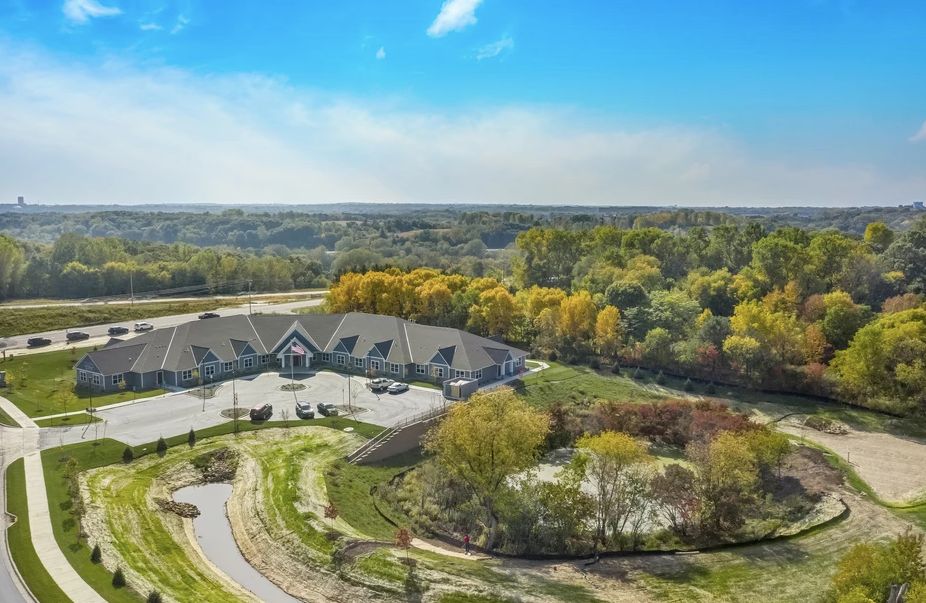Aerial view of a building surrounded by lush greenery and roads, with a clear blue sky overhead.