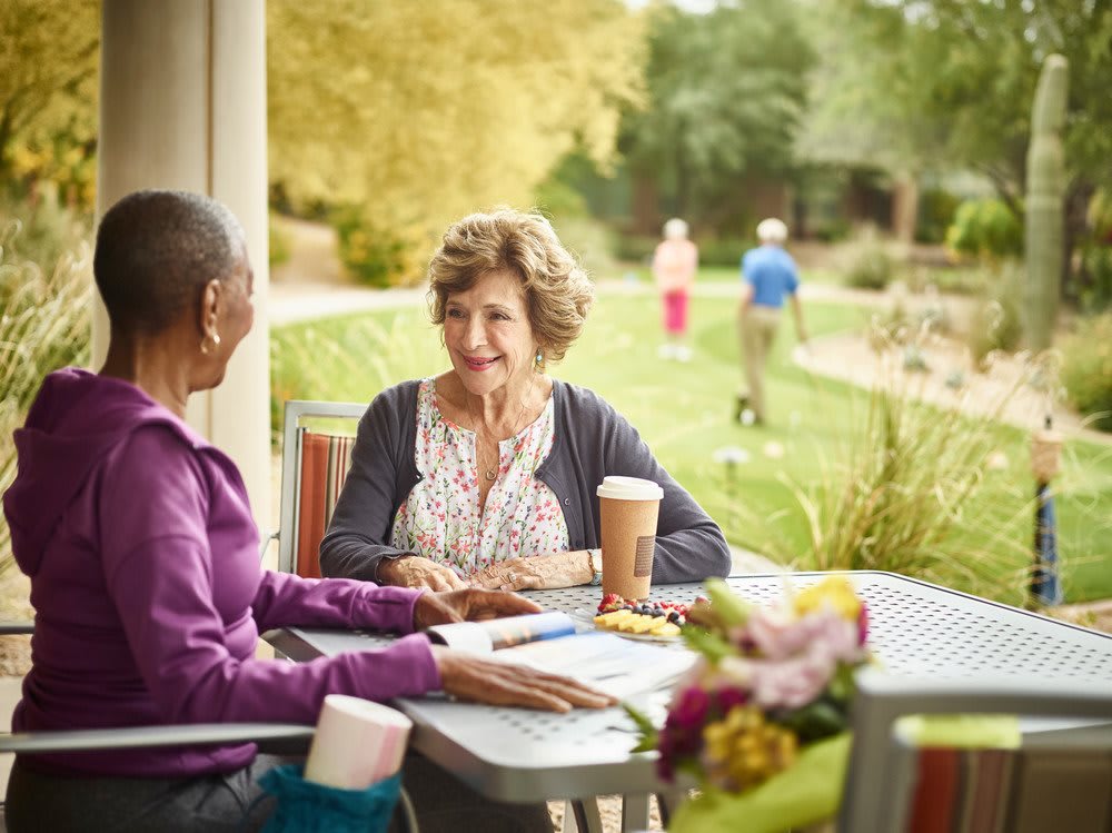 Two seniors enjoying a conversation over coffee in a garden setting.