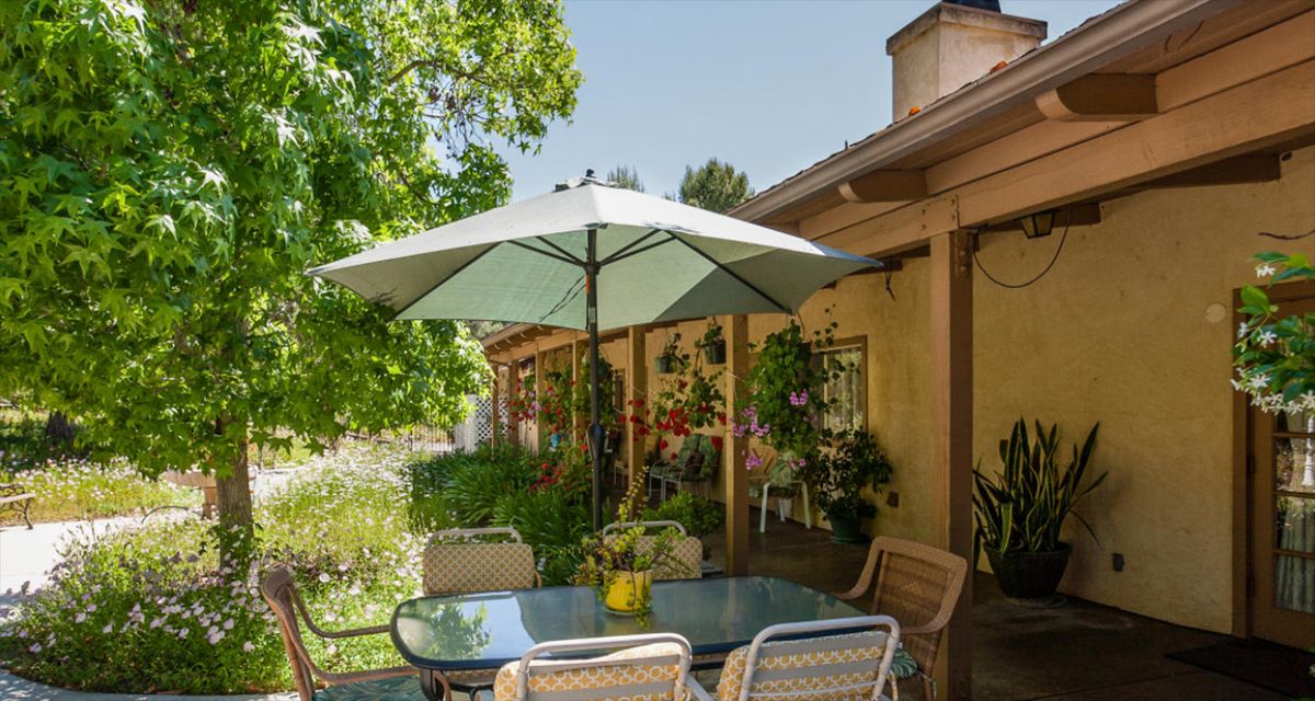 A cozy patio with a shaded umbrella, surrounded by lush greenery and outdoor seating.