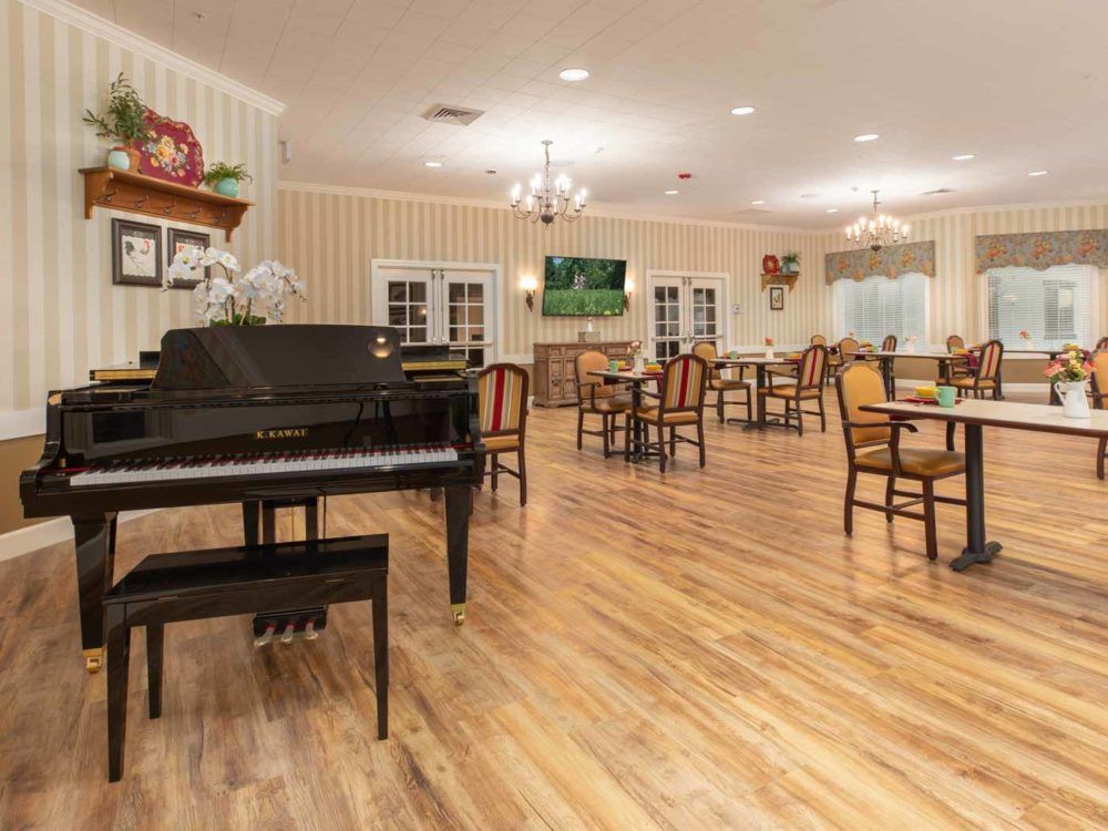 A spacious dining area with a piano, featuring wooden floors and elegant chandeliers.