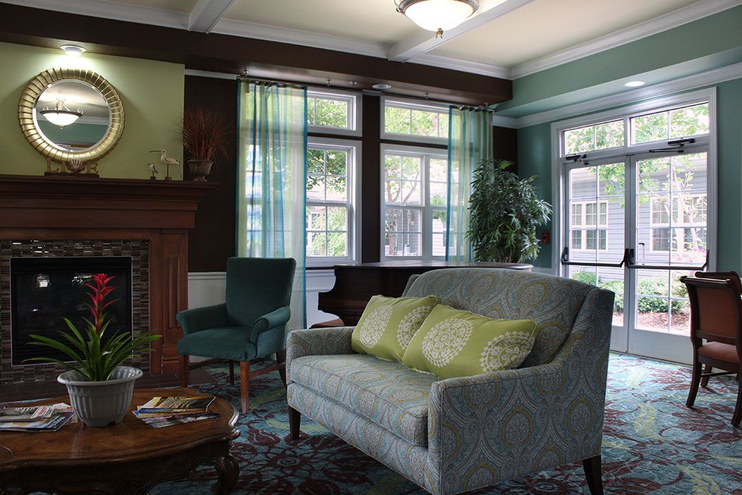 A cozy living room with natural light, featuring a sofa, armchair, and fireplace.