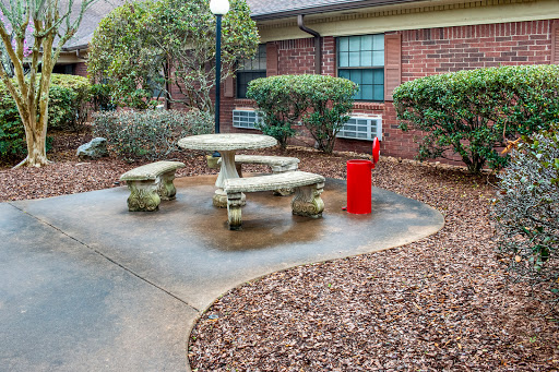 A serene outdoor seating area with a stone picnic table and benches, surrounded by landscaped plants and a striking red object.