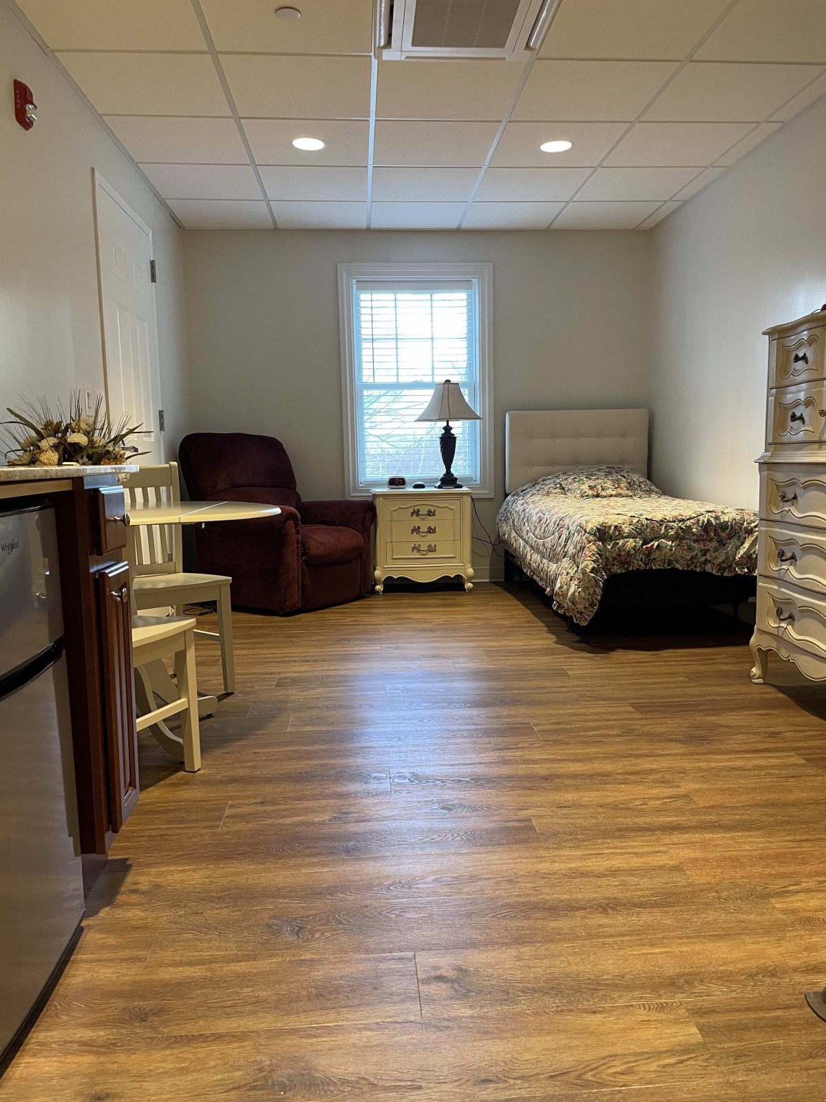 A cozy bedroom with a single bed, armchair, and a small dining table.