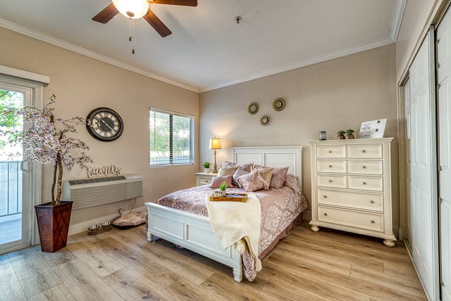 A cozy bedroom with a white bed, dresser, and decorative elements under a ceiling fan.