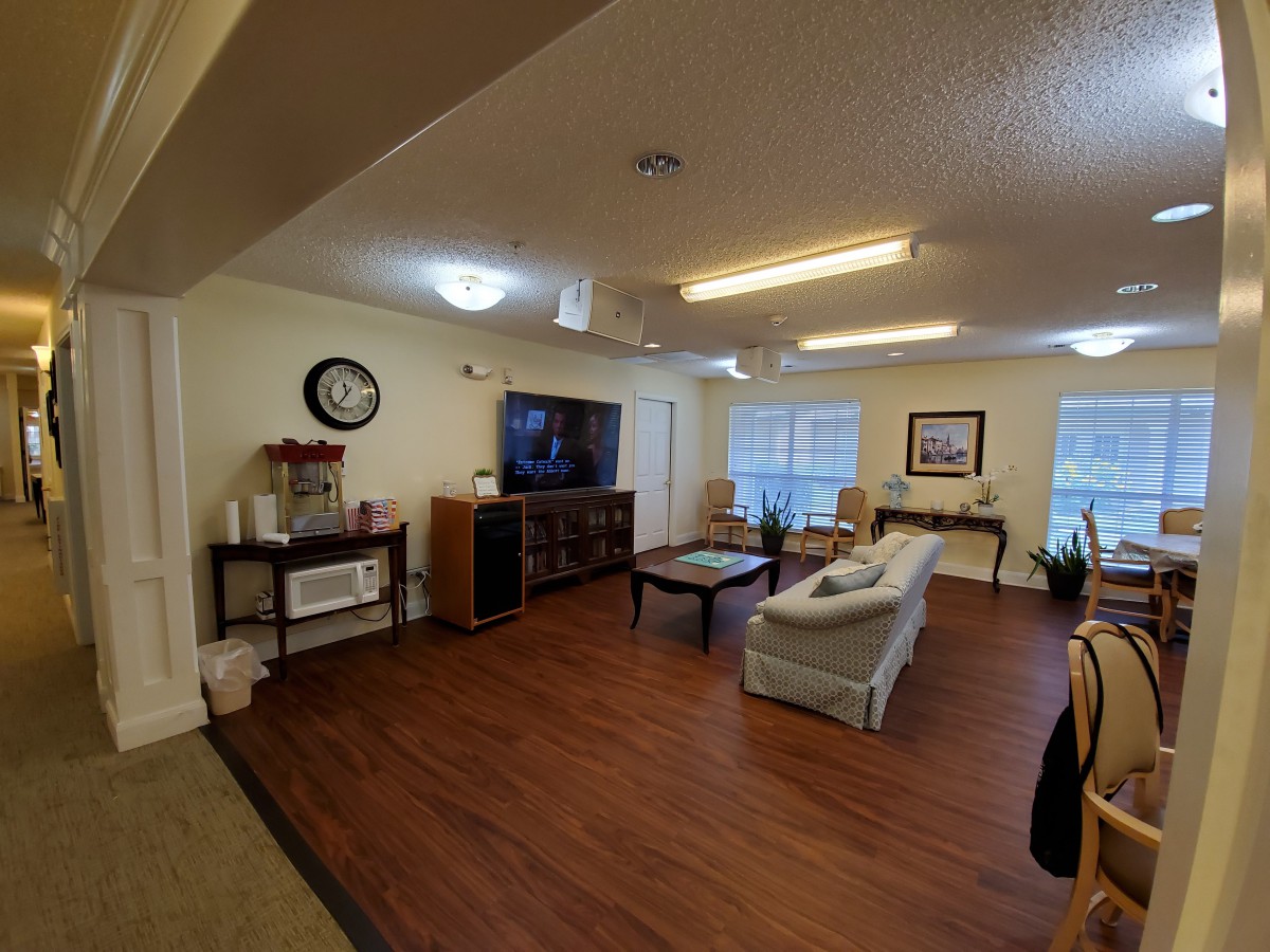 A cozy living room featuring a sofa, coffee table, and a television with wood flooring and large windows.