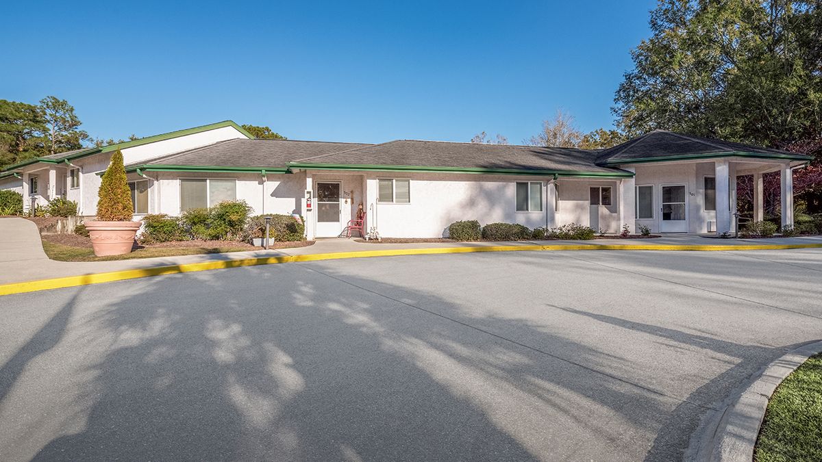 A suburban single-story building with a parking lot in front, captured on a clear sunny day.
