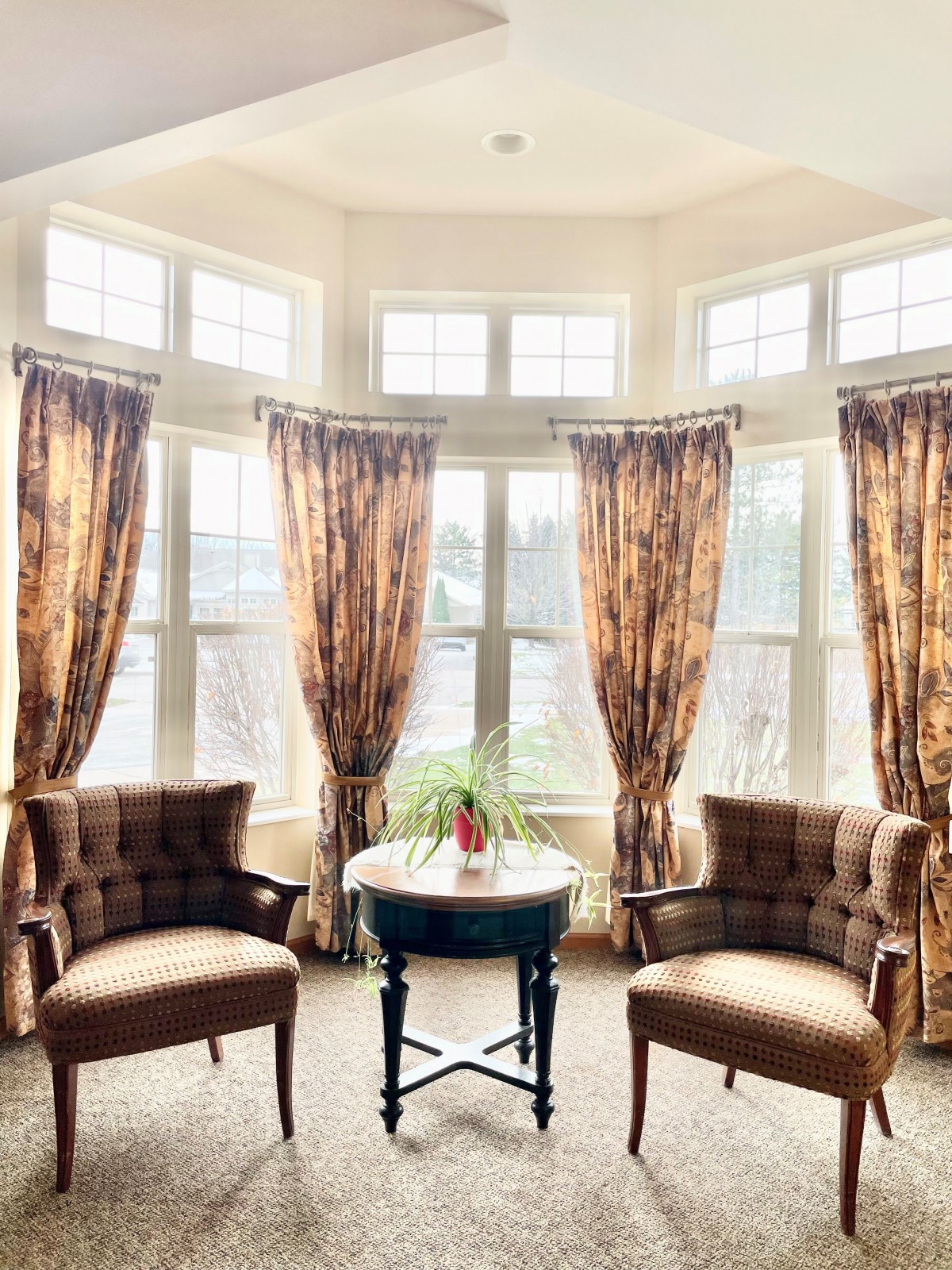 A cozy sitting area with two chairs and a table in front of a sunlit bay window.