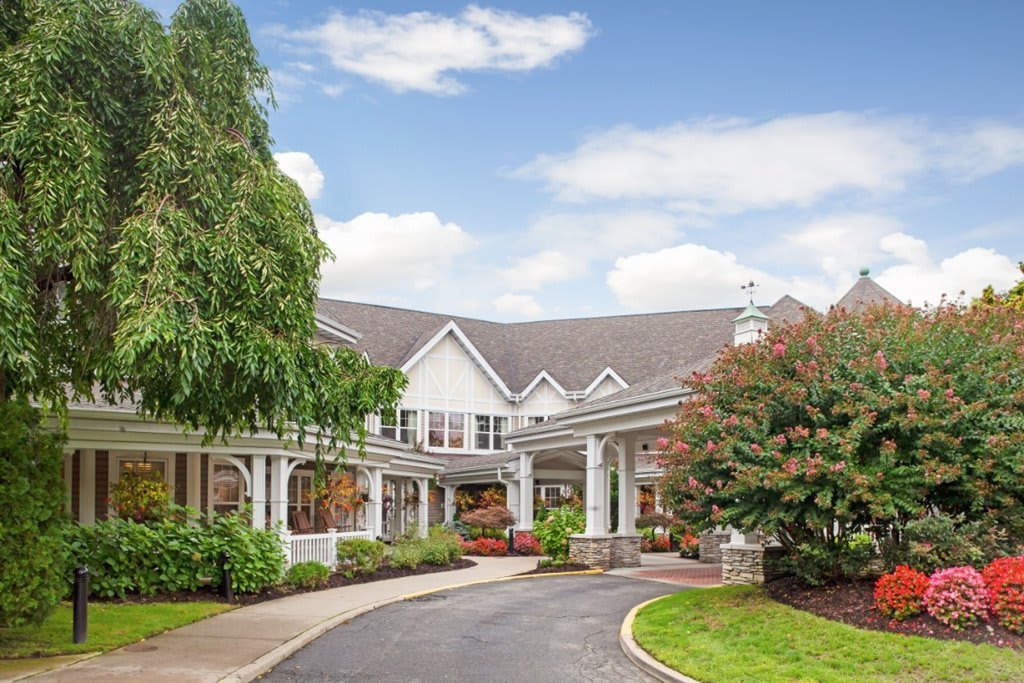 A picturesque residential building with a driveway surrounded by lush greenery and a clear sky.