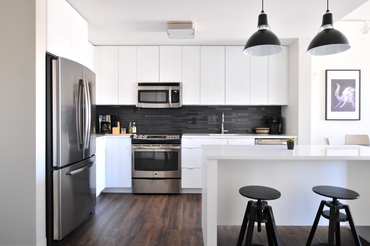 A modern kitchen with white cabinets, stainless steel appliances, and a black backsplash.