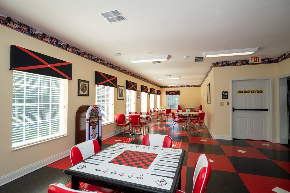 A retro-themed diner room with red and black decor, featuring a jukebox, checkered flooring, and game tables.