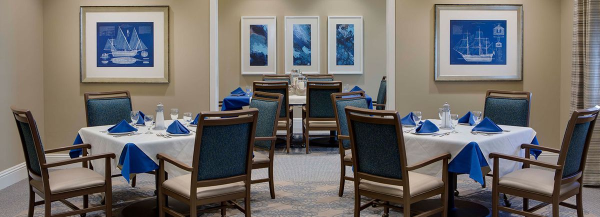A formal dining room with neatly arranged chairs and tables, adorned with blue-themed artwork on the walls.