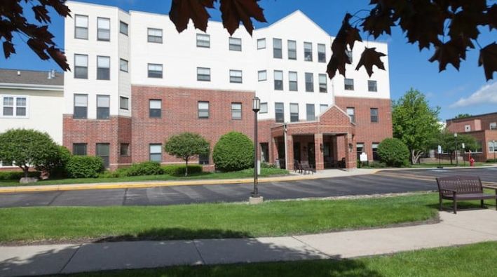A multi-story residential building with a brick facade and an entrance canopy, surrounded by landscaped greenery.