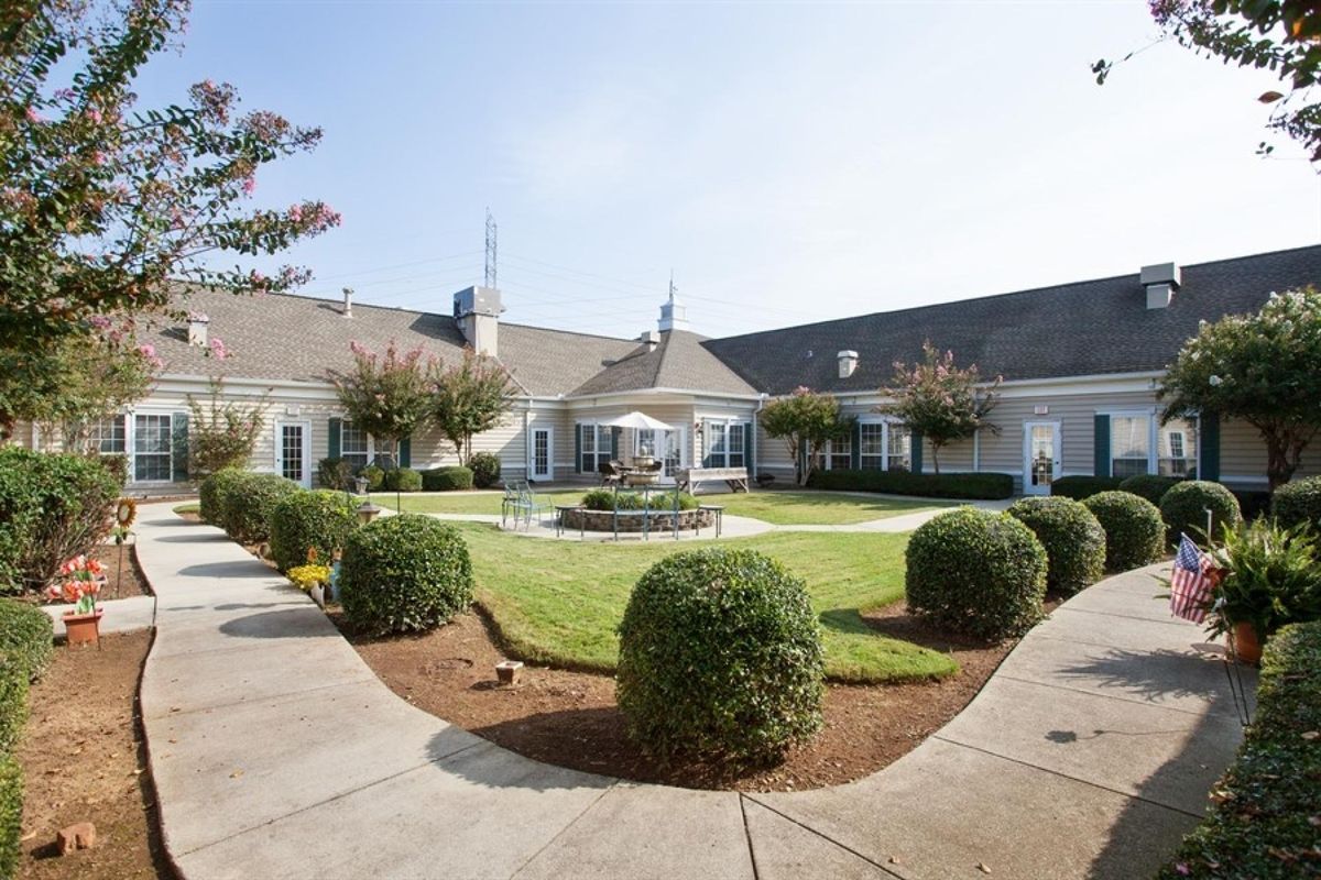 A beautifully landscaped courtyard with a central fountain and surrounding pathways in front of a large building.