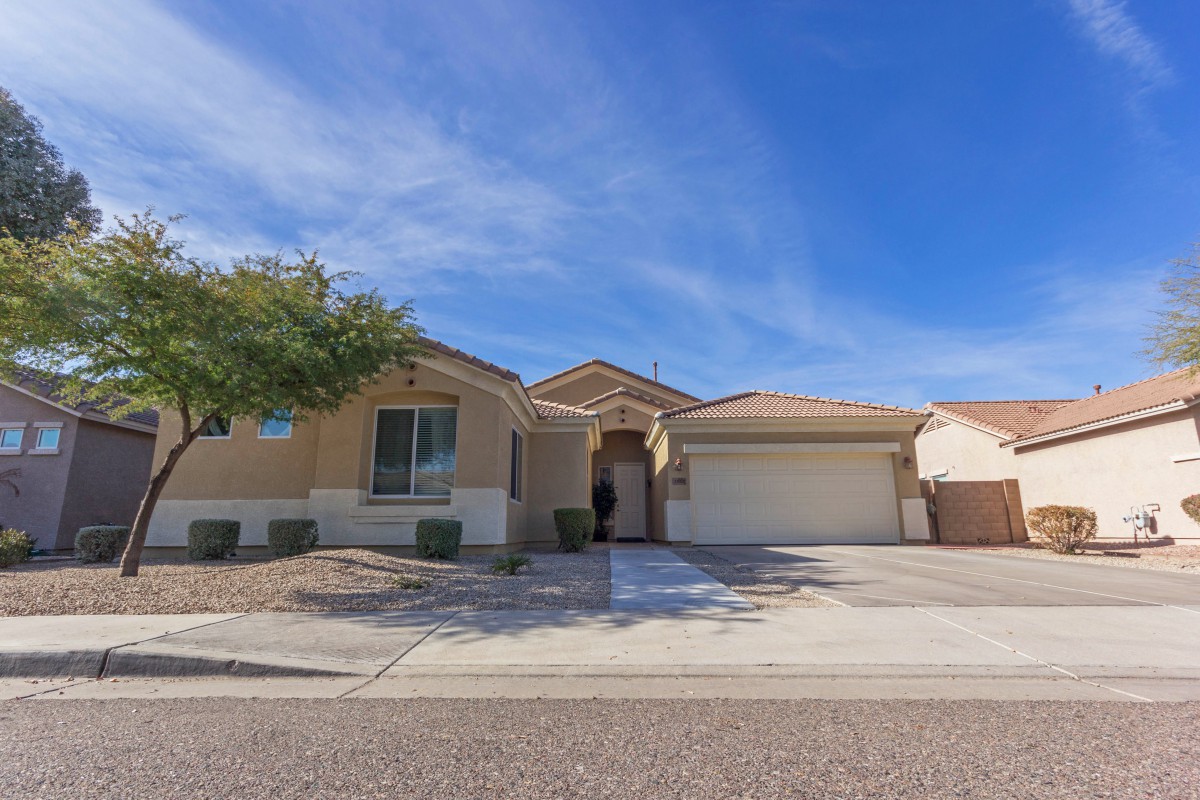 A single-story suburban house with a driveway and garage, set against a clear blue sky.