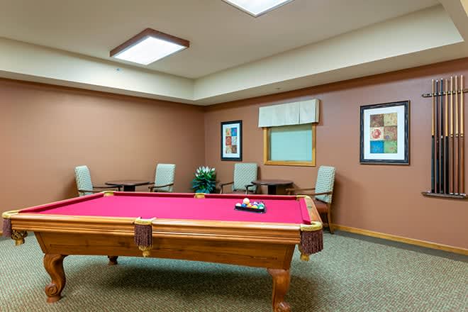 A cozy game room featuring a red pool table surrounded by chairs.