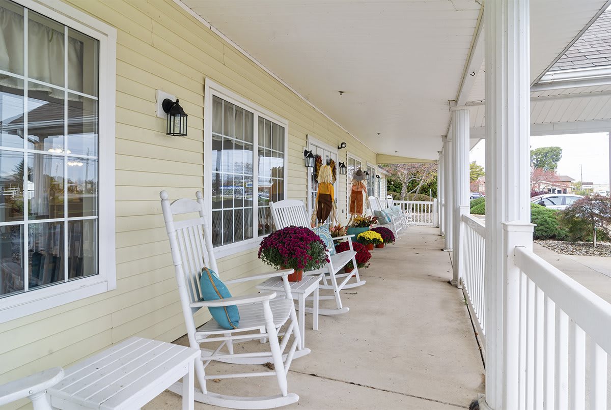 A cozy porch with white rocking chairs and colorful flowers along a yellow house.