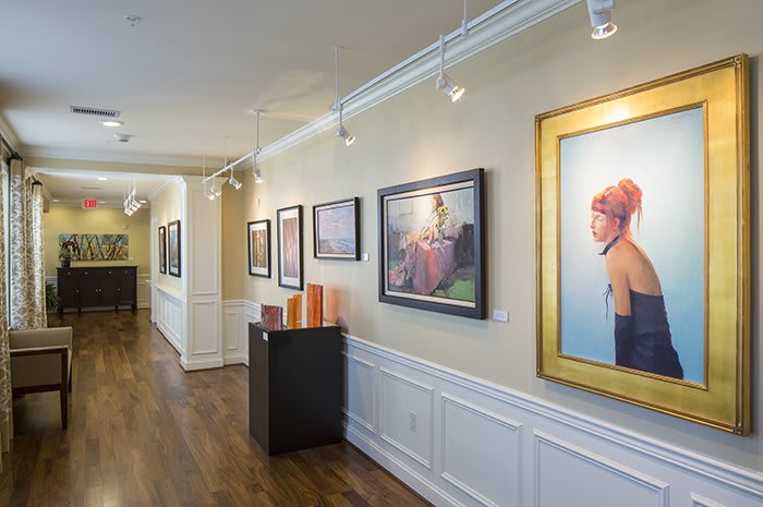 A well-lit art gallery showcasing a variety of paintings along a corridor.
