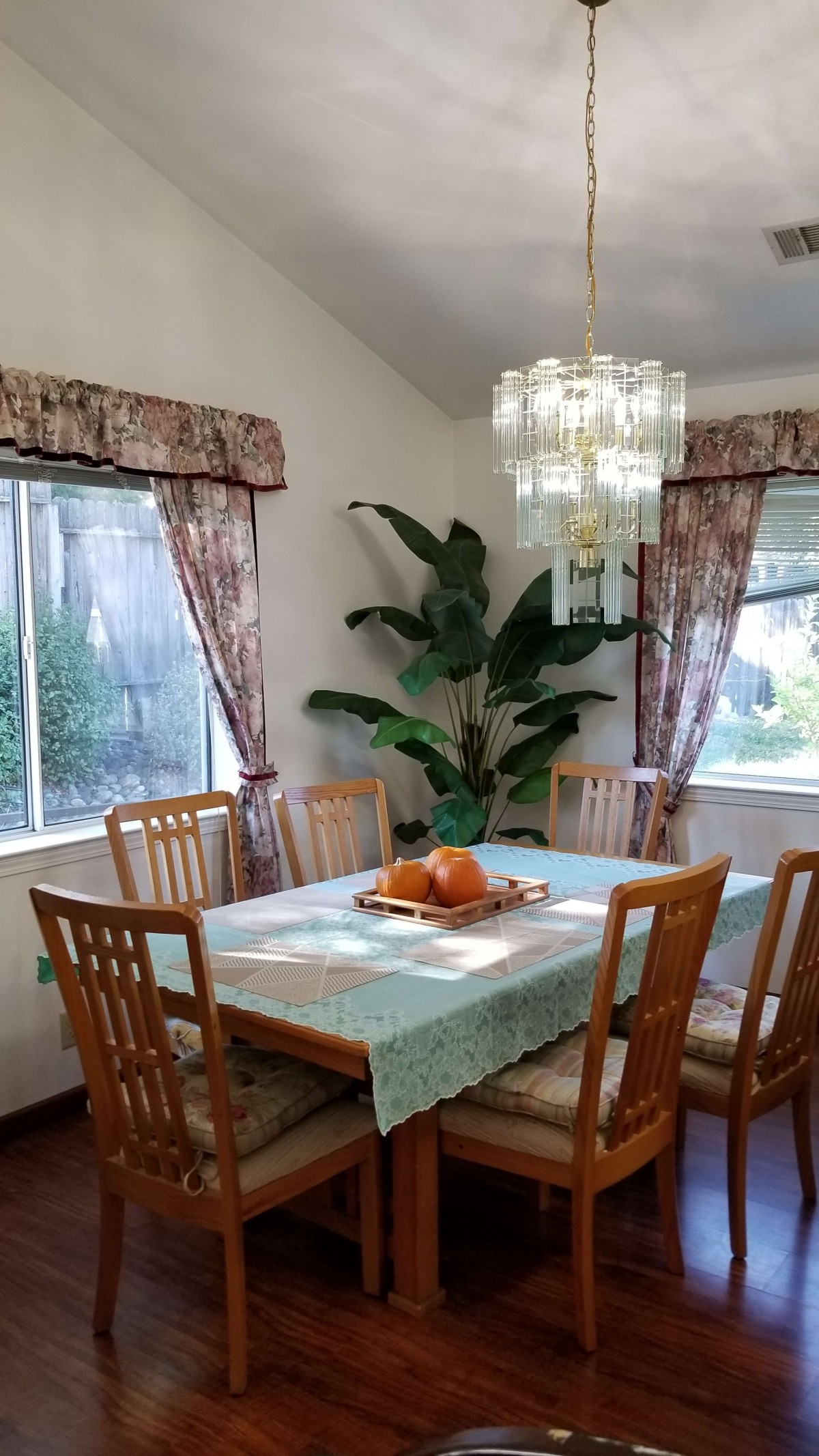 A cozy dining room with a table set for a meal, surrounded by wooden chairs and brightened by natural light filtering through the windows.