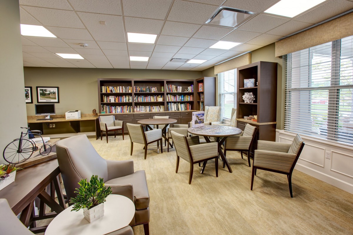 A cozy library seating area with bookshelves, tables, and chairs.