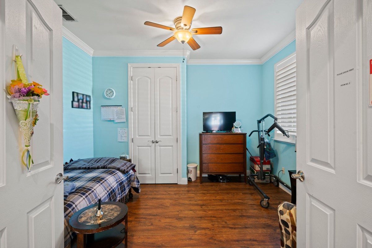 A cozy bedroom with blue walls, featuring a bed, dresser, TV, and ceiling fan.