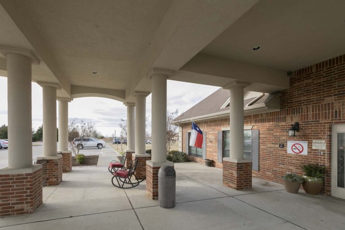 A covered entrance area with columns and outdoor seating, featuring a flag near a brick building.