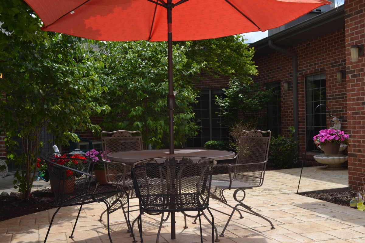 A sunny patio with a table, chairs, and a large red umbrella.