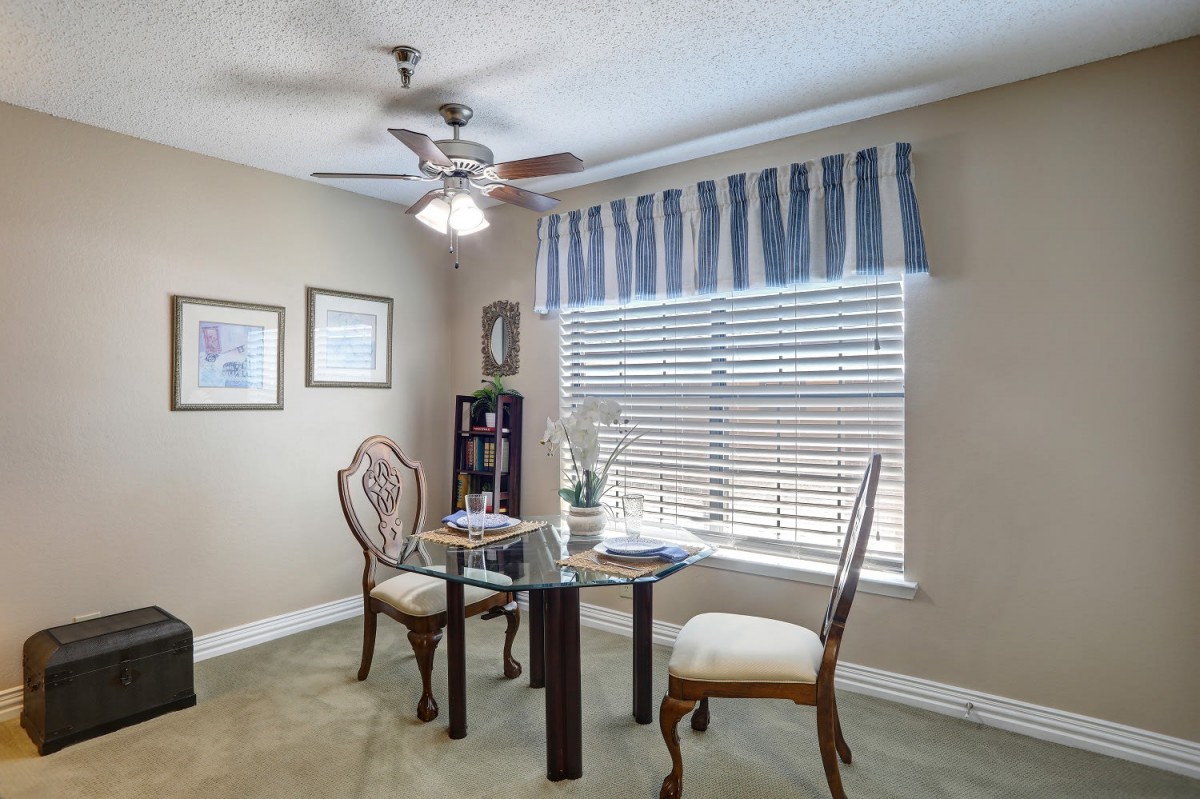 A cozy dining area with a round glass table, elegant chairs, and a window draped with striped curtains.