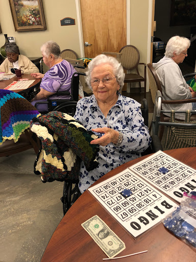 An elderly woman proudly displays a knitted blanket during a bingo game at a community center.