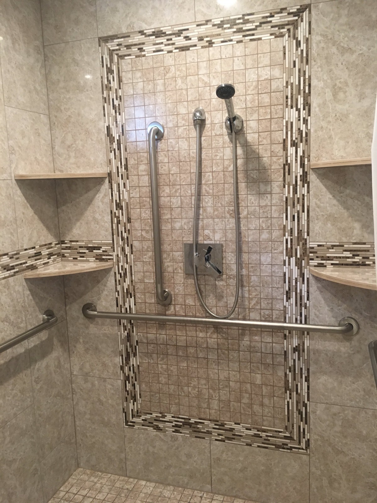 A tiled shower with multiple showerheads and built-in shelves, featuring a grab bar for safety.