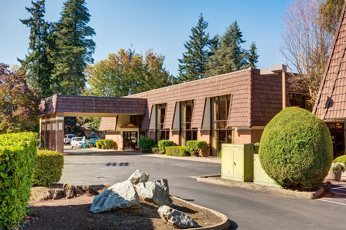 A modern building surrounded by trees with a parking area in the foreground.