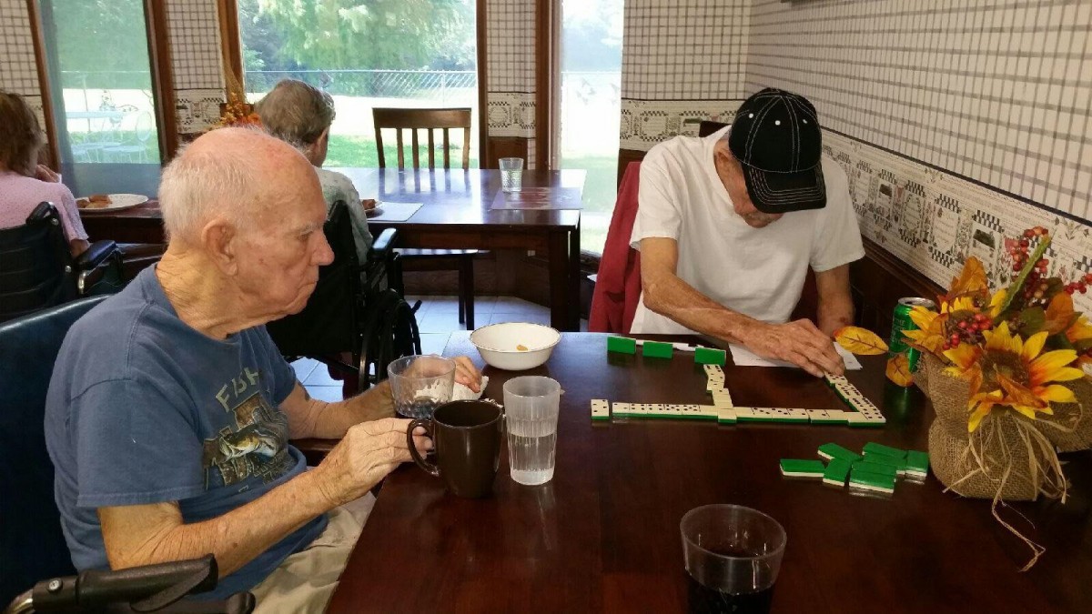 Elderly individuals sitting at a table enjoying drinks and playing a game.