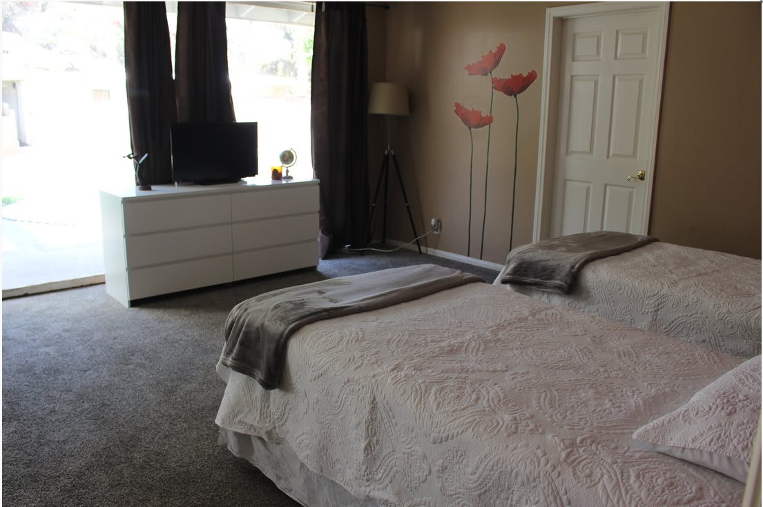 A modern bedroom with twin beds, a dresser, and a wall-mounted TV.