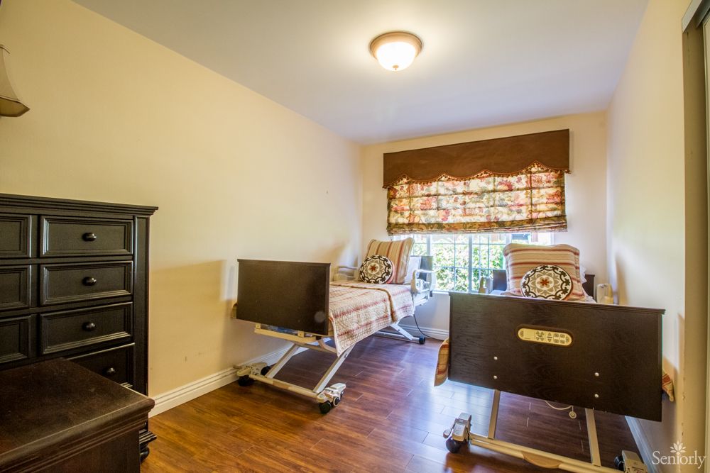 A cozy bedroom featuring hospital beds, wooden flooring, and a window with curtains.