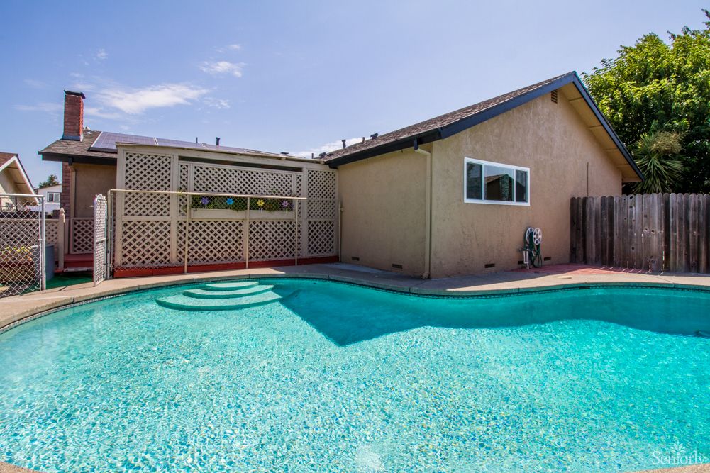 A backyard with a swimming pool and a house under a clear blue sky.