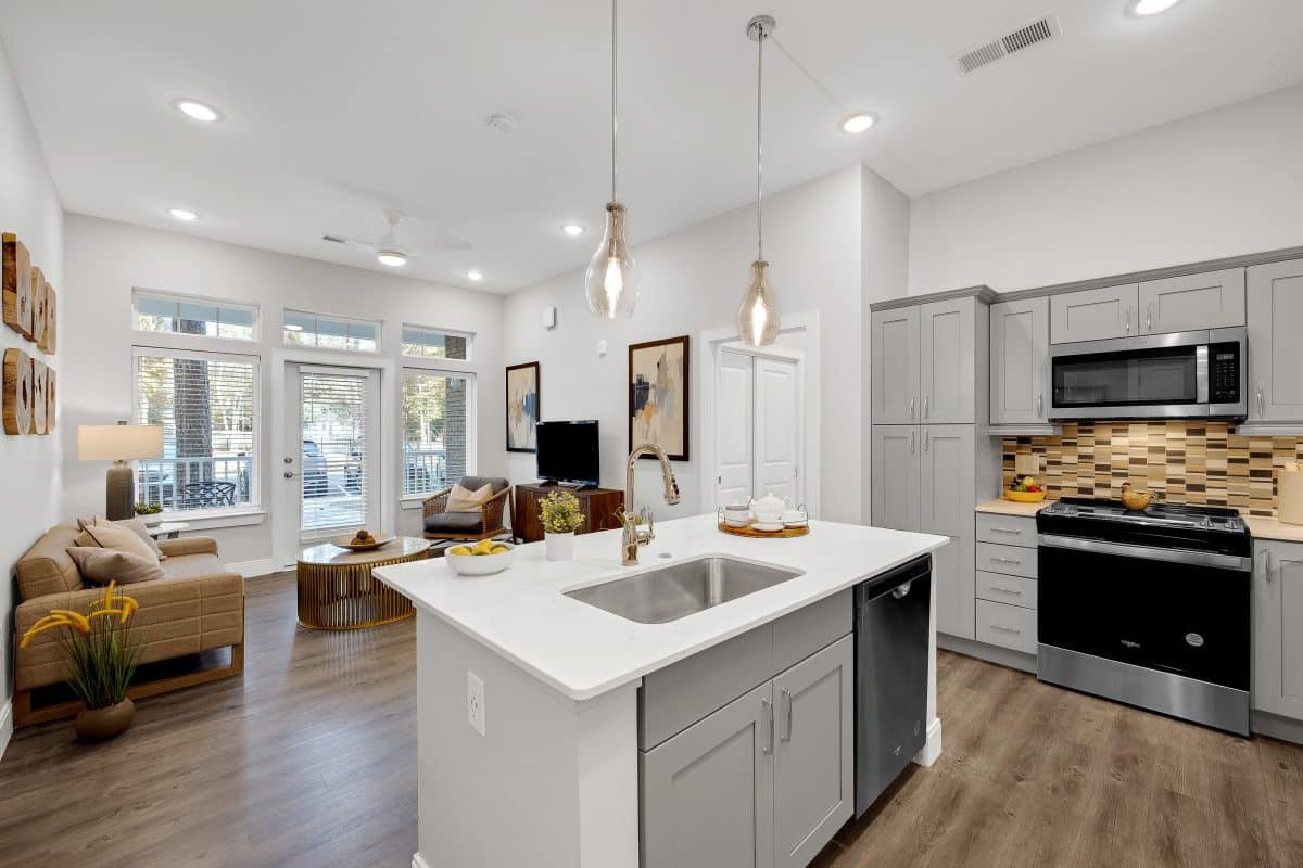 A modern open-concept kitchen and living area with sleek design elements, featuring an island counter, pendant lights, and hardwood flooring.