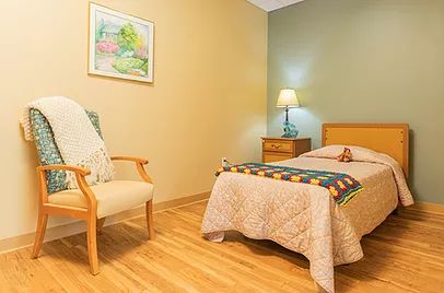 A cozy bedroom with a single bed, lamp, and wooden floor.