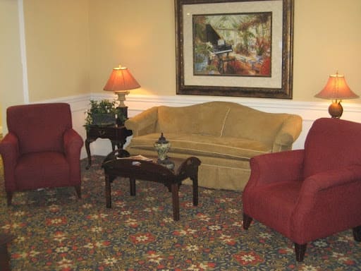 A cozy living room with a sofa, two armchairs, a coffee table, and a lamp, adorned by a painting on the wall.
