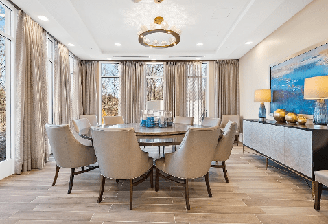 A modern dining room with a round table, upholstered chairs, and an elegant chandelier.