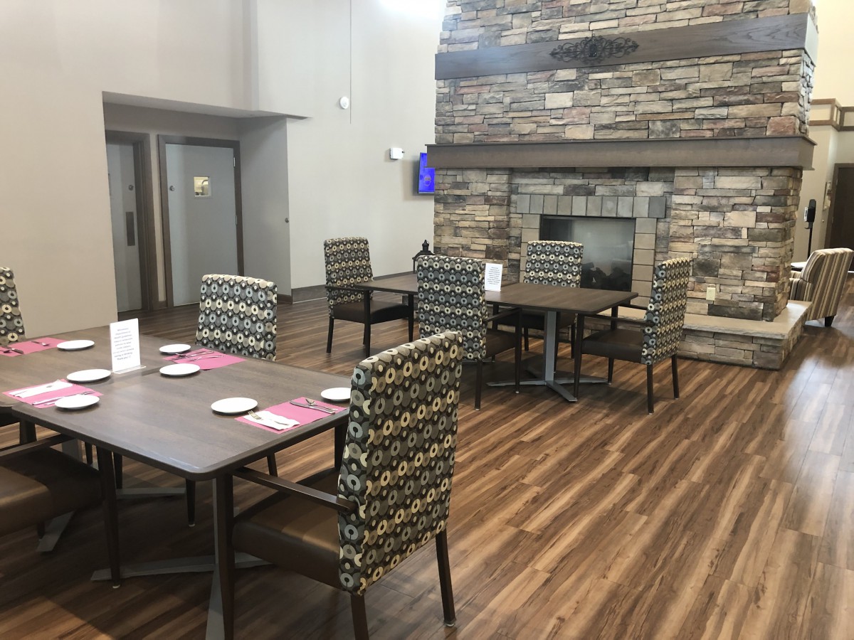 A cozy dining area with tables and chairs, featuring a stone fireplace and wooden flooring.
