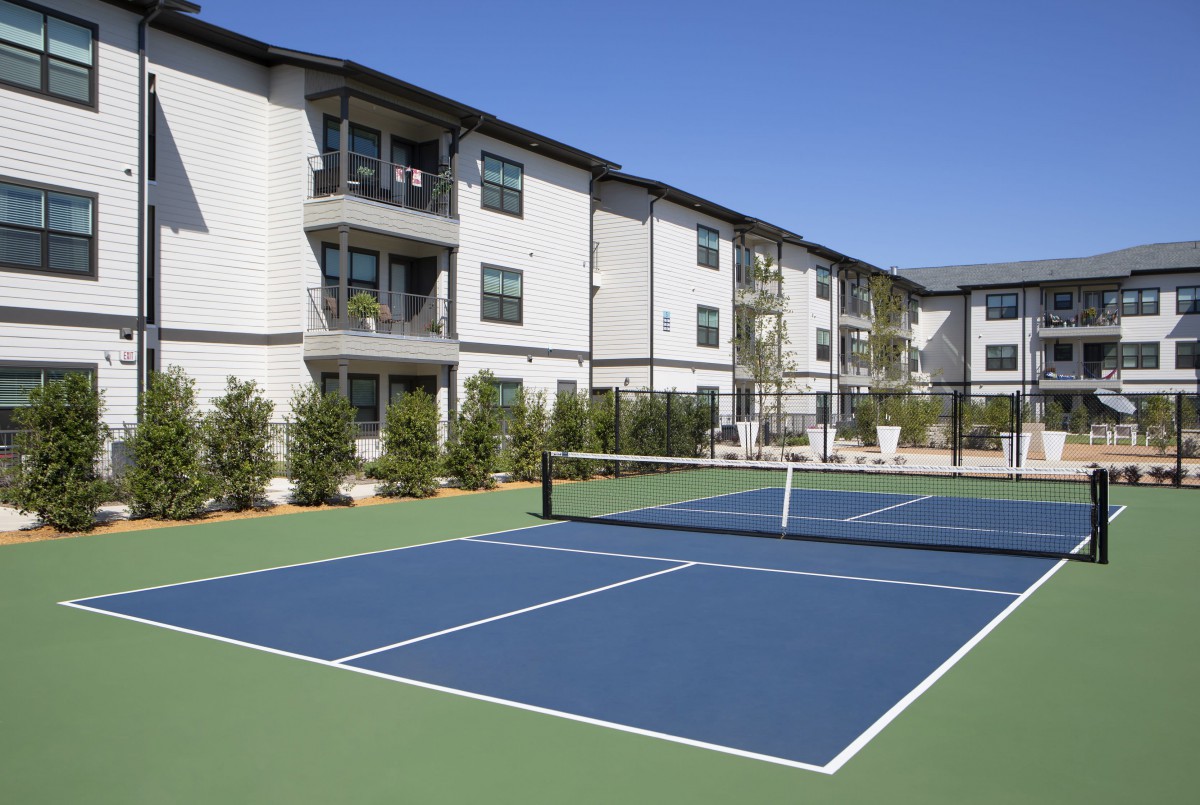 Outdoor tennis court in front of a modern apartment complex.