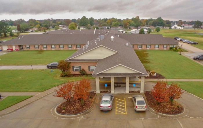 Aerial view of a senior living facility with a landscaped entrance and parked cars.