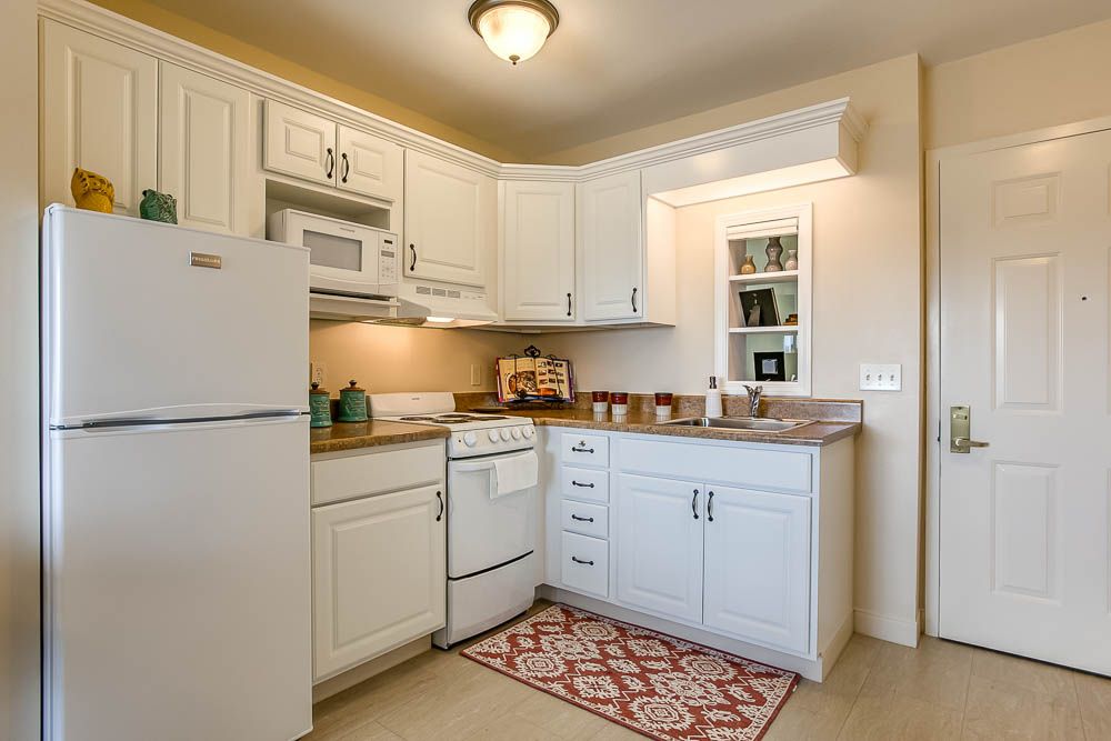 A cozy kitchen with white cabinets, modern appliances, and a decorative rug.