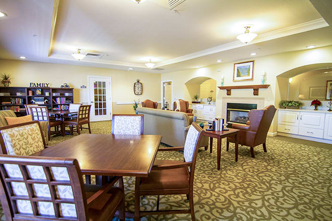 A cozy interior space with dining tables and chairs, featuring a living room area with a carpeted floor.