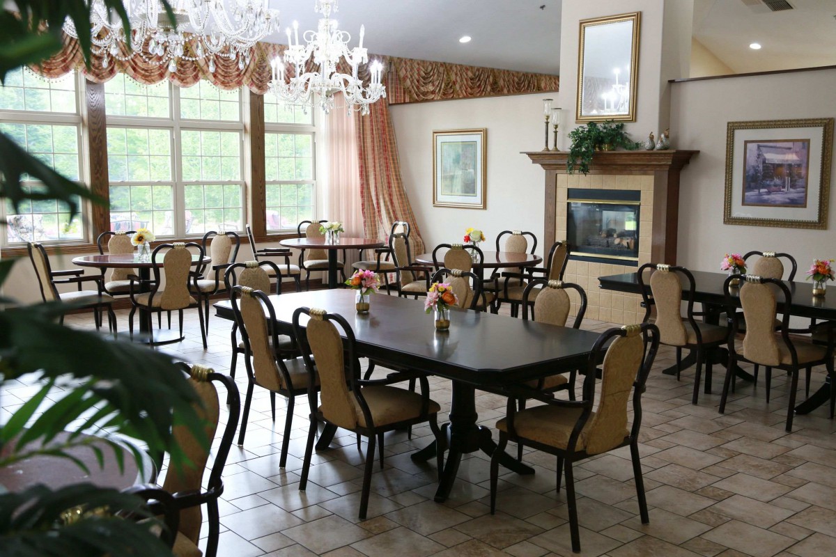 A well-lit dining area with neatly arranged tables and chairs, featuring a chandelier and a fireplace.