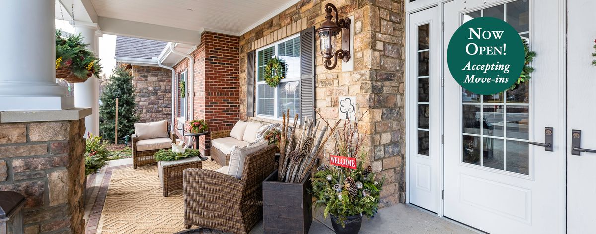 A cozy porch with wicker furniture and decorative plants against a stone and brick wall.