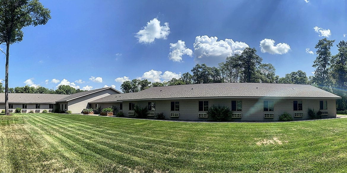 A panoramic view of a residential house with a well-maintained lawn under a clear blue sky.