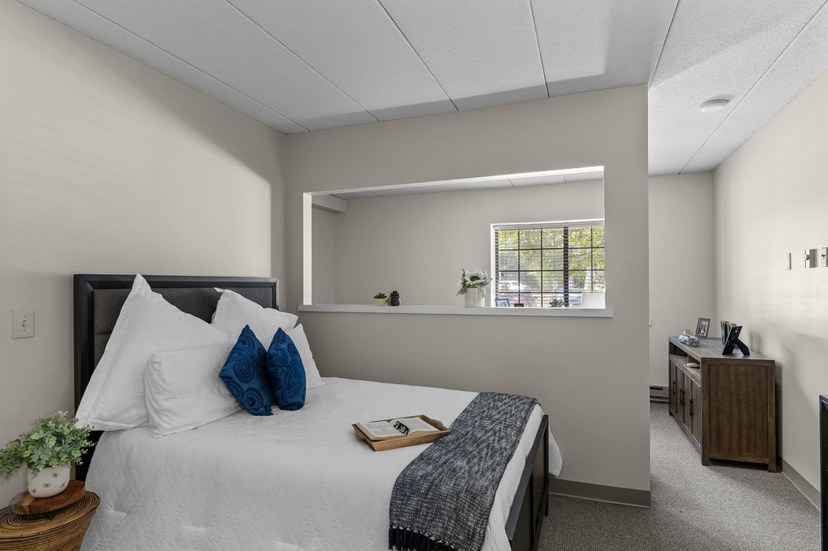 A modern bedroom with a neatly made bed and decorative pillows, featuring a window and a neutral color scheme.