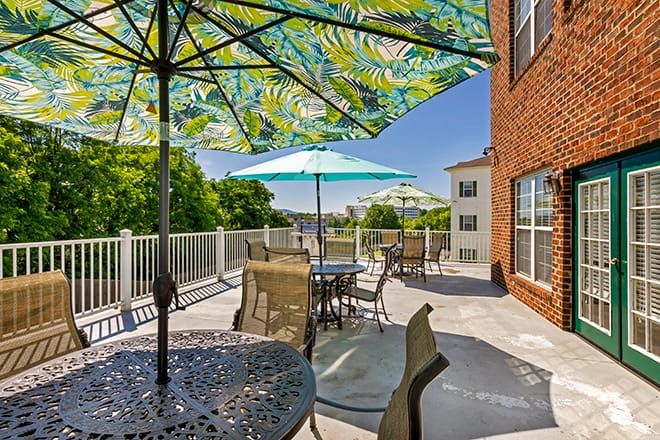A sunlit patio with colorful umbrellas, tables, and chairs next to a brick building.