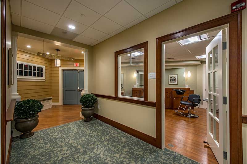 A cozy interior space with a waiting area and salon, featuring wooden floors, carpet, and potted plants.